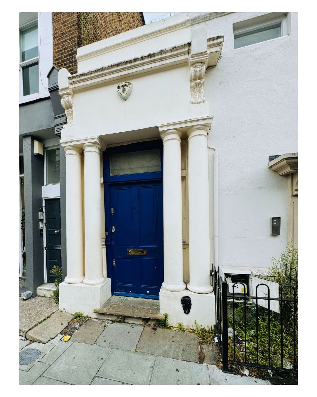 Auto-generated description: Une porte d'entrée bleue est encadrée par quatre colonnes blanches avec un décor architectural classique sur une façade blanche.
