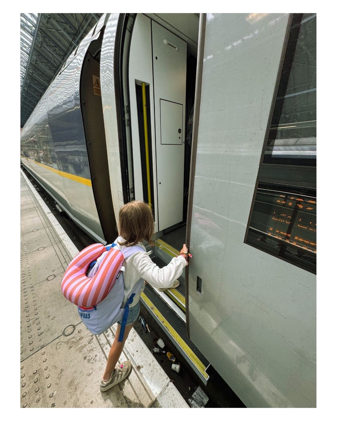 Auto-generated description: Une petite fille avec un sac à dos coloré monte à bord d'un train à quai.