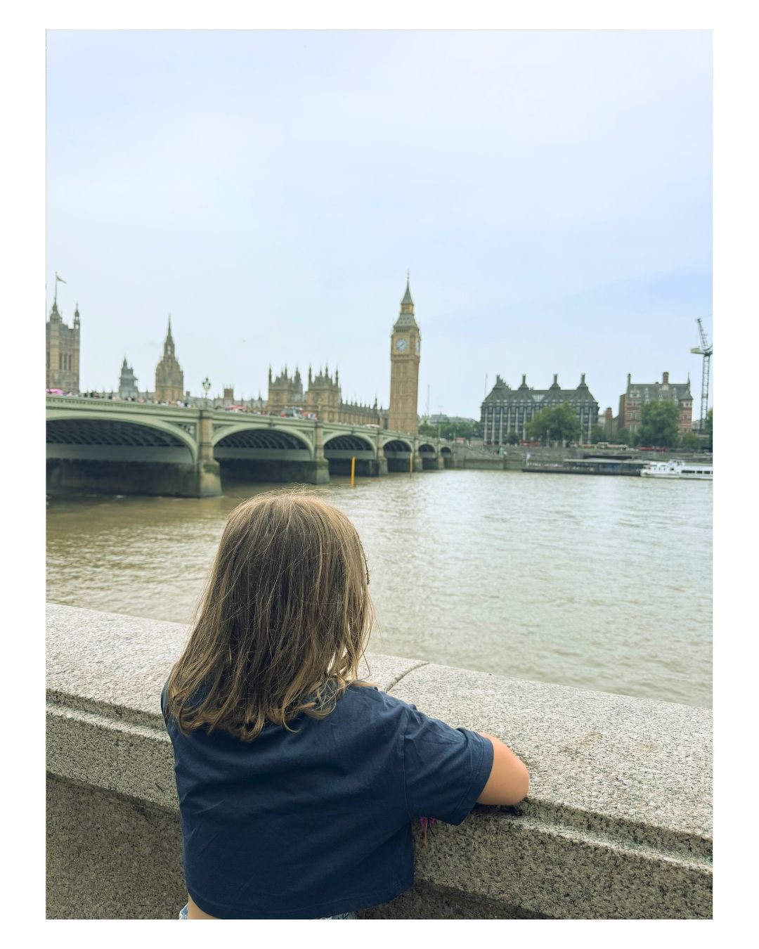 Auto-generated description: Un enfant regarde la Tamise avec le pont de Westminster et la tour Elizabeth (Big Ben) en arrière-plan à Londres.