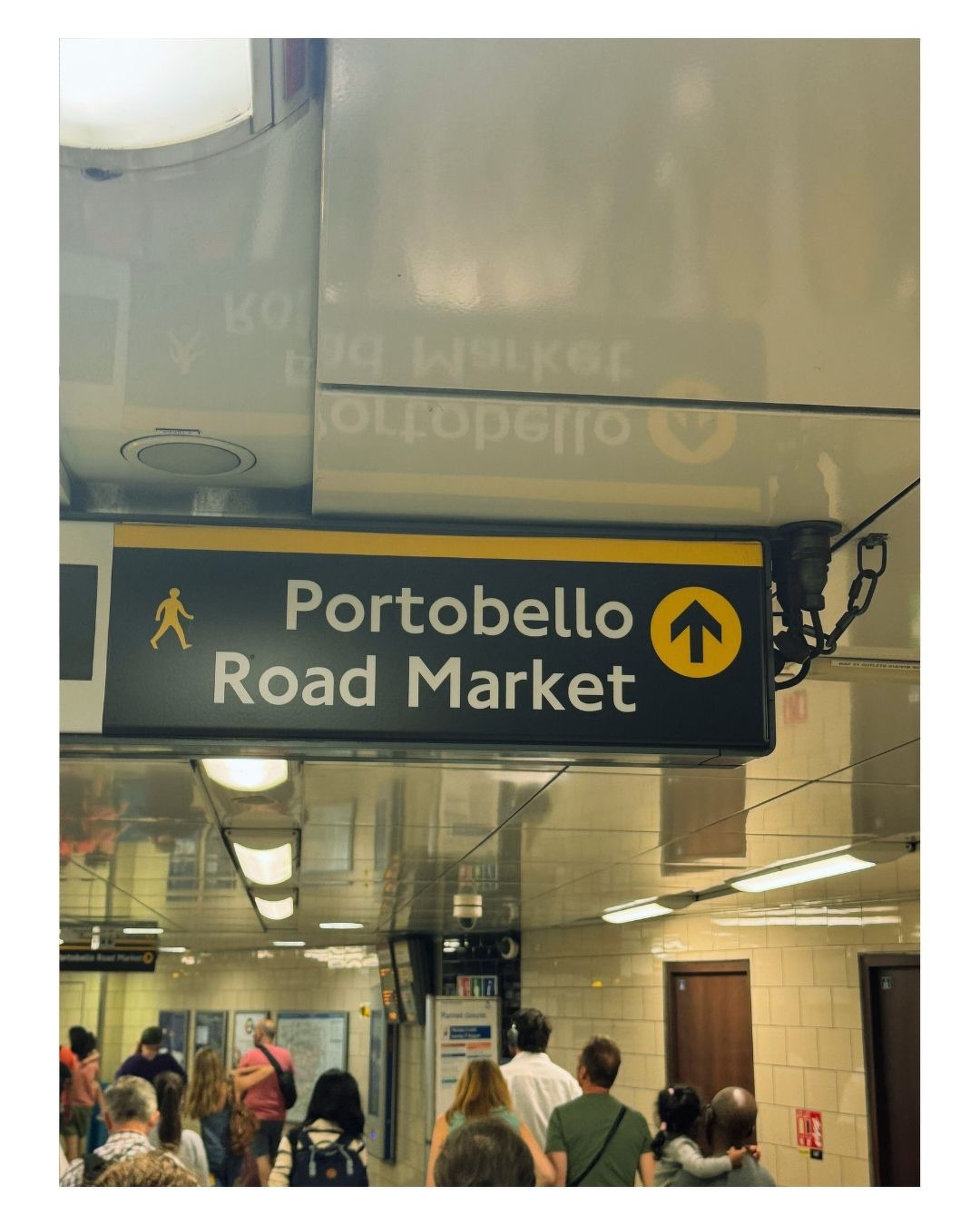 Auto-generated description: Un panneau indique la direction vers le marché de Portobello Road dans une station de métro animée.