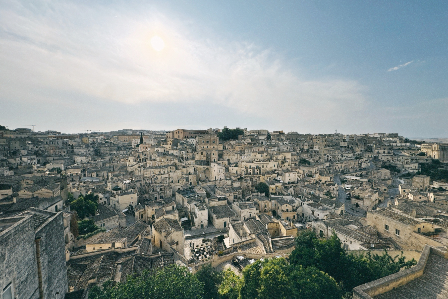 Auto-generated description: Un village ancien et dense avec des maisons en pierre de couleur claire sous un ciel clair avec un soleil brillant.