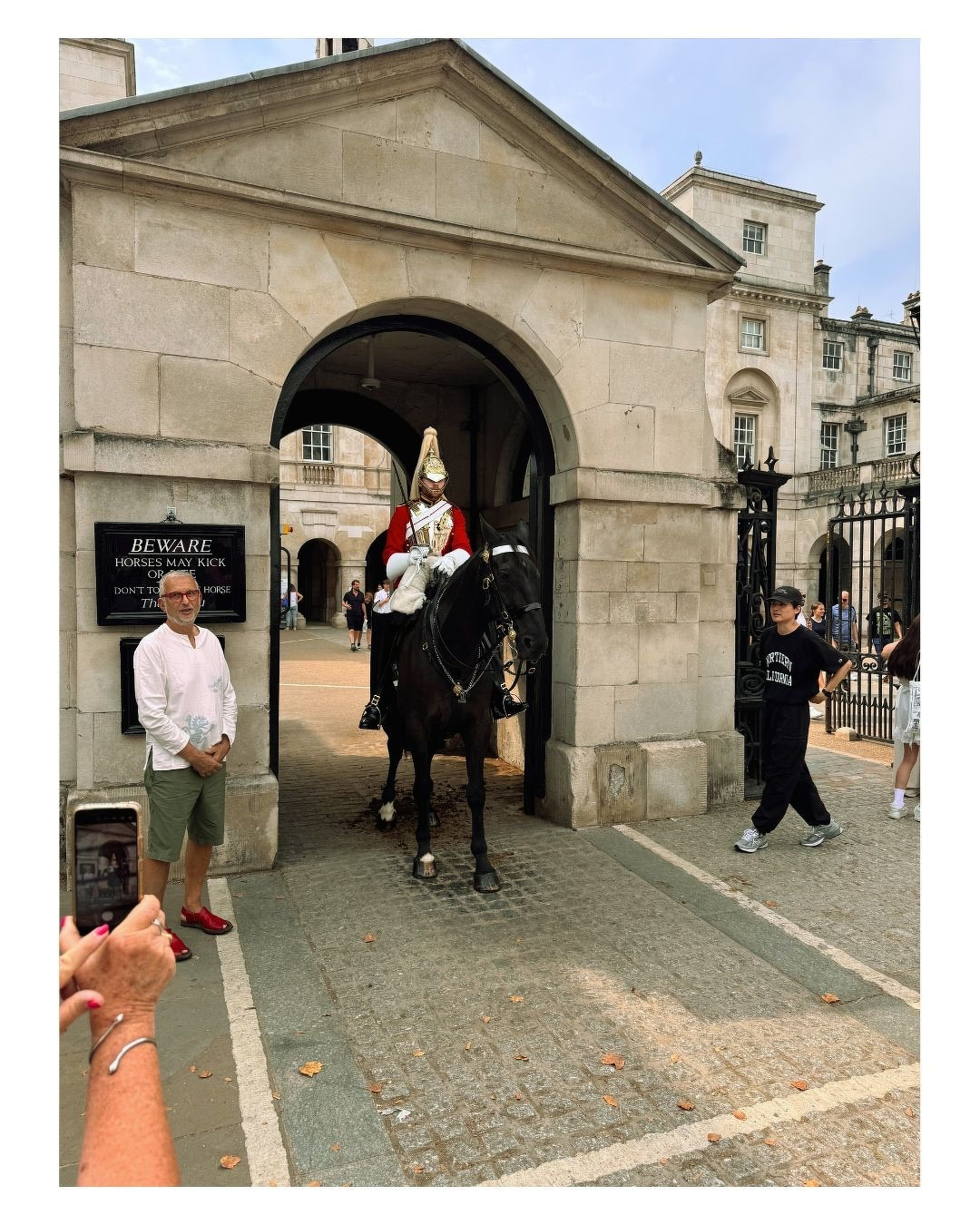 Auto-generated description: Un soldat en uniforme historique est à cheval sous une arche en pierre, entouré de passants qui prennent des photos.
