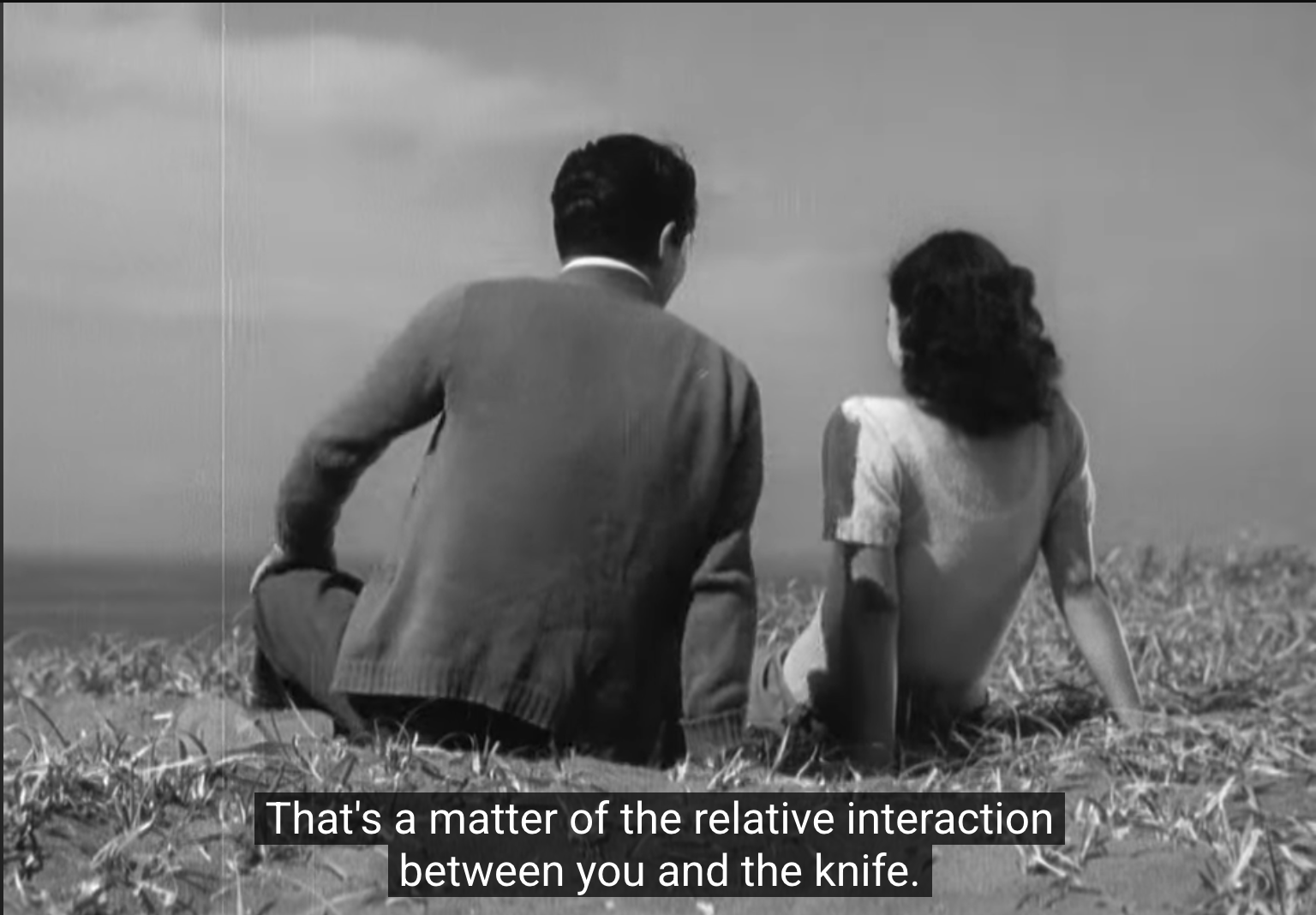 a still from ozu's "late spring" of noriko (setsuko hara) and hattori (jun usami) at the beach. the shot is from behind and hattori is saying "that's a matter of relative interaction between you and the knife."