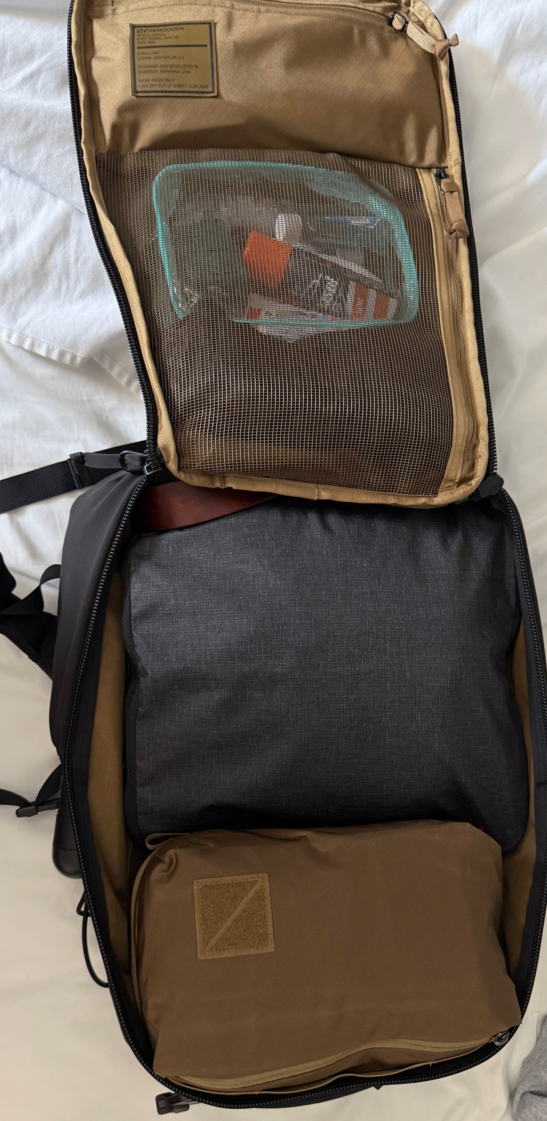 A backpack is opened to show neatly packed items, including a transparent pouch with toiletries and various compartments.
