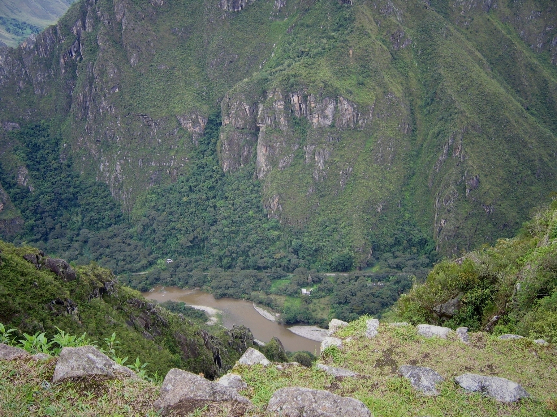 A rocky cliff overlooks a winding river surrounded by dense, green forest and tall, rugged mountains covered in vegetation.