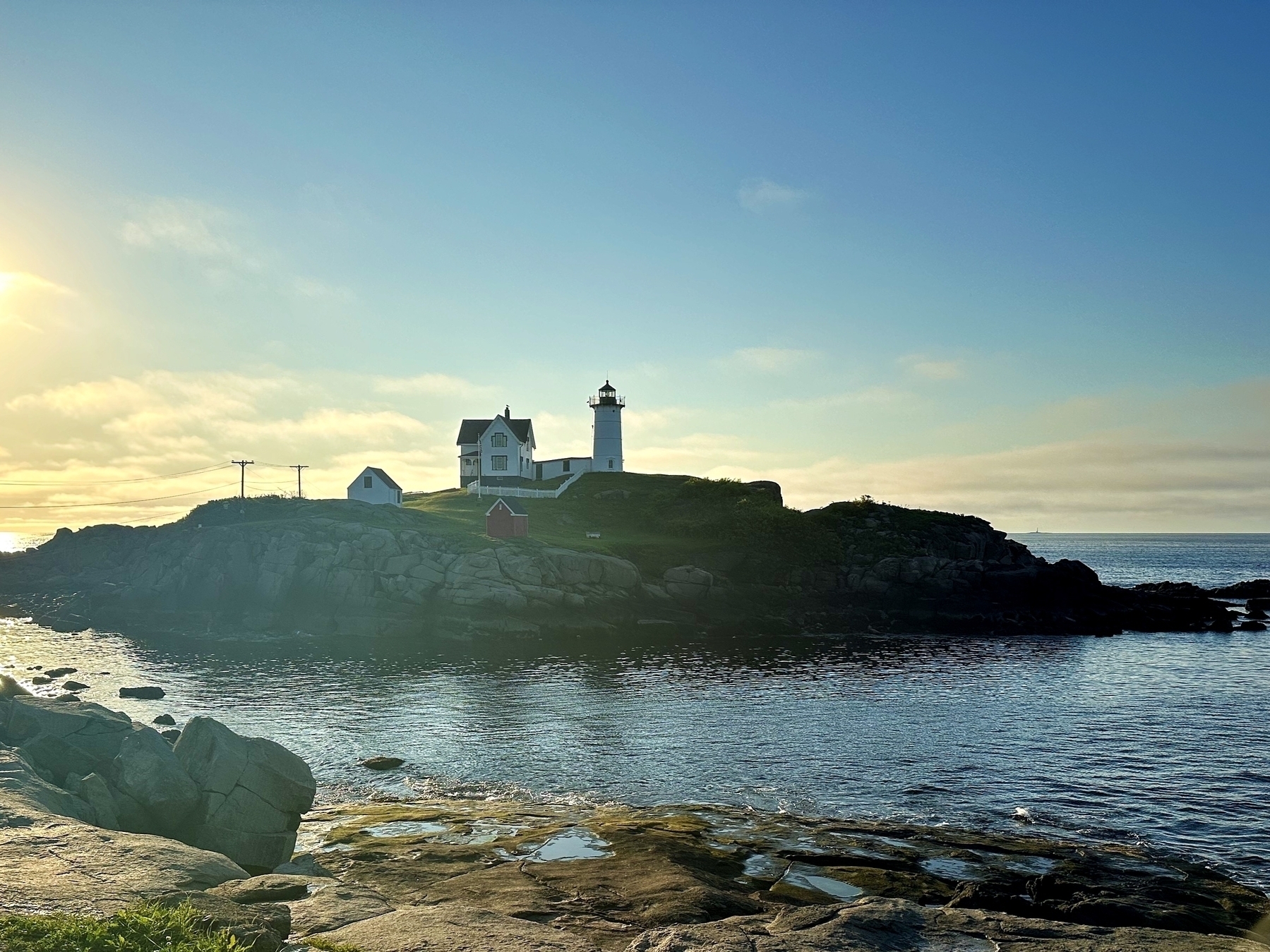 Lighthouse standing on a rocky coastal hill under a clear blue sky with the ocean and an unobstructed horizon in the background during daylight.