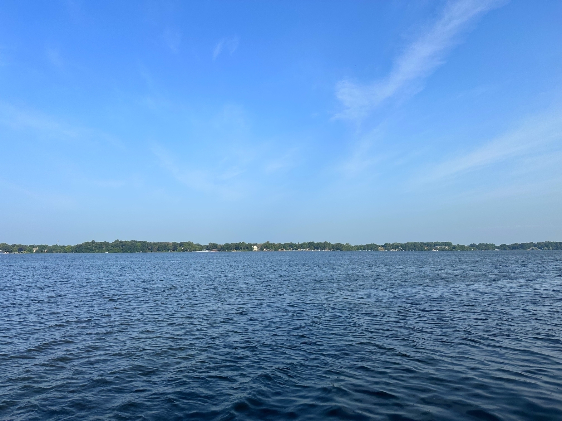 A still lake lies beneath a clear blue sky, with a distant treeline forming the horizon.