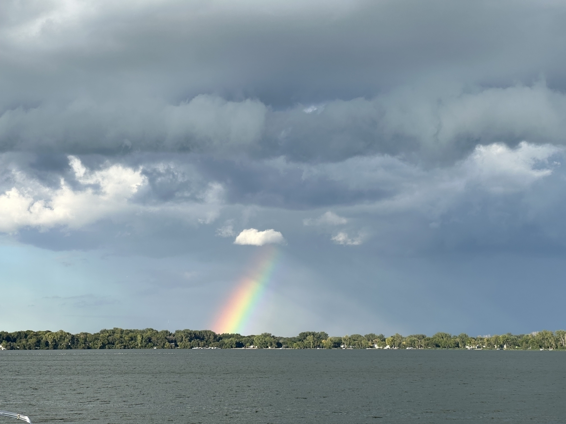 A rainbow arcs over a body of water beneath a cloudy sky.