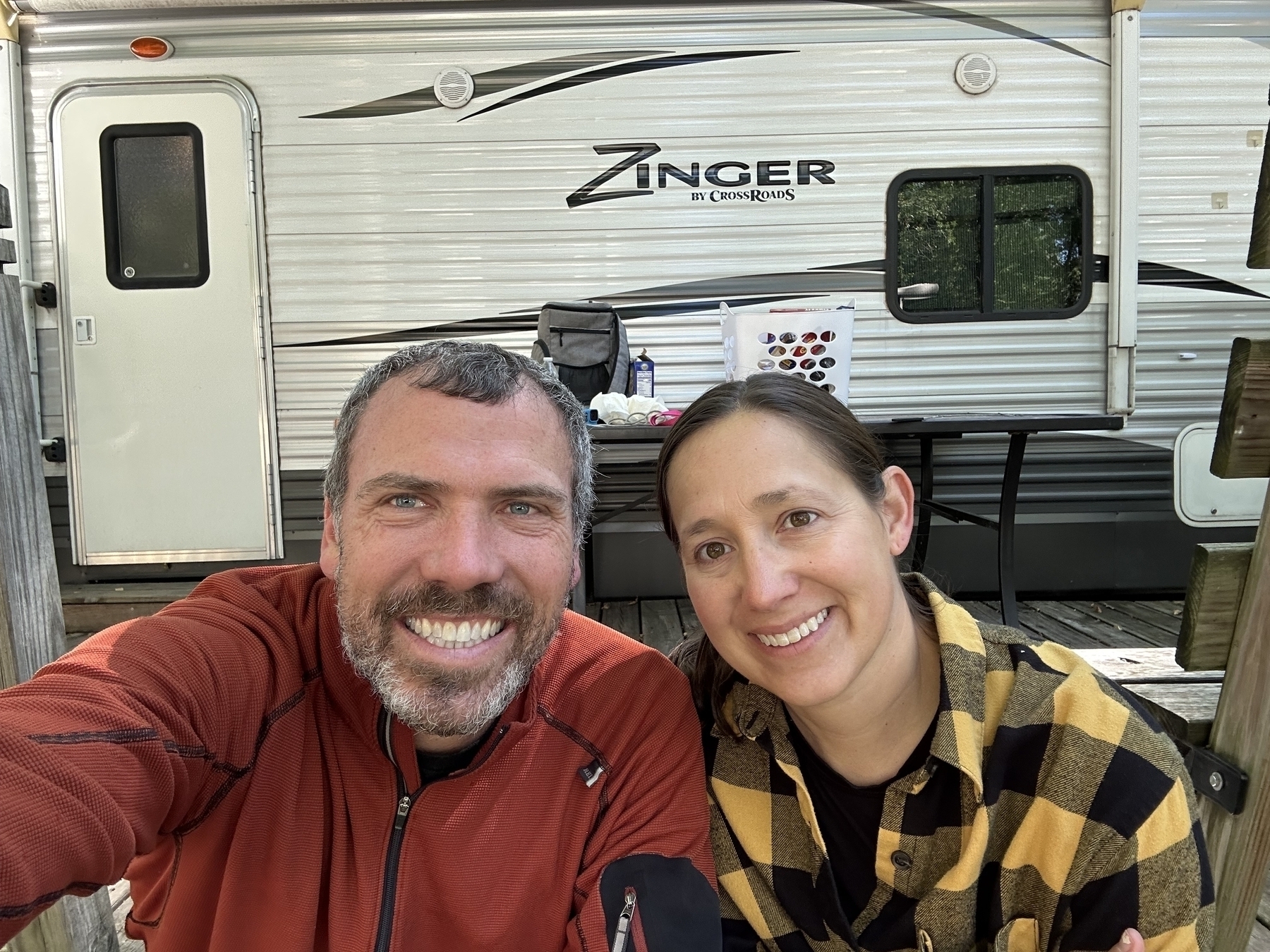 A man and woman are smiling in front of a Zinger RV