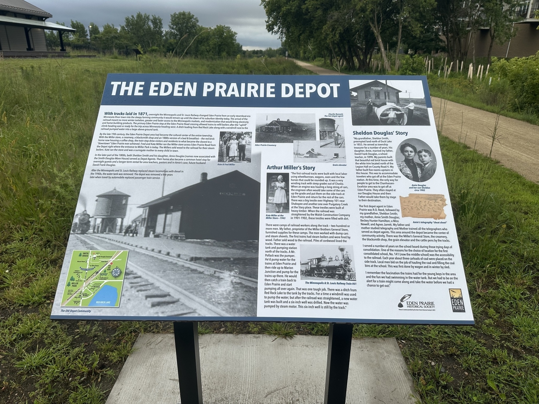 Interpretive sign titled “The Eden Prairie Depot” with historical information, images, and a map, located in a grassy area with a gravel path leading through trees in the background.