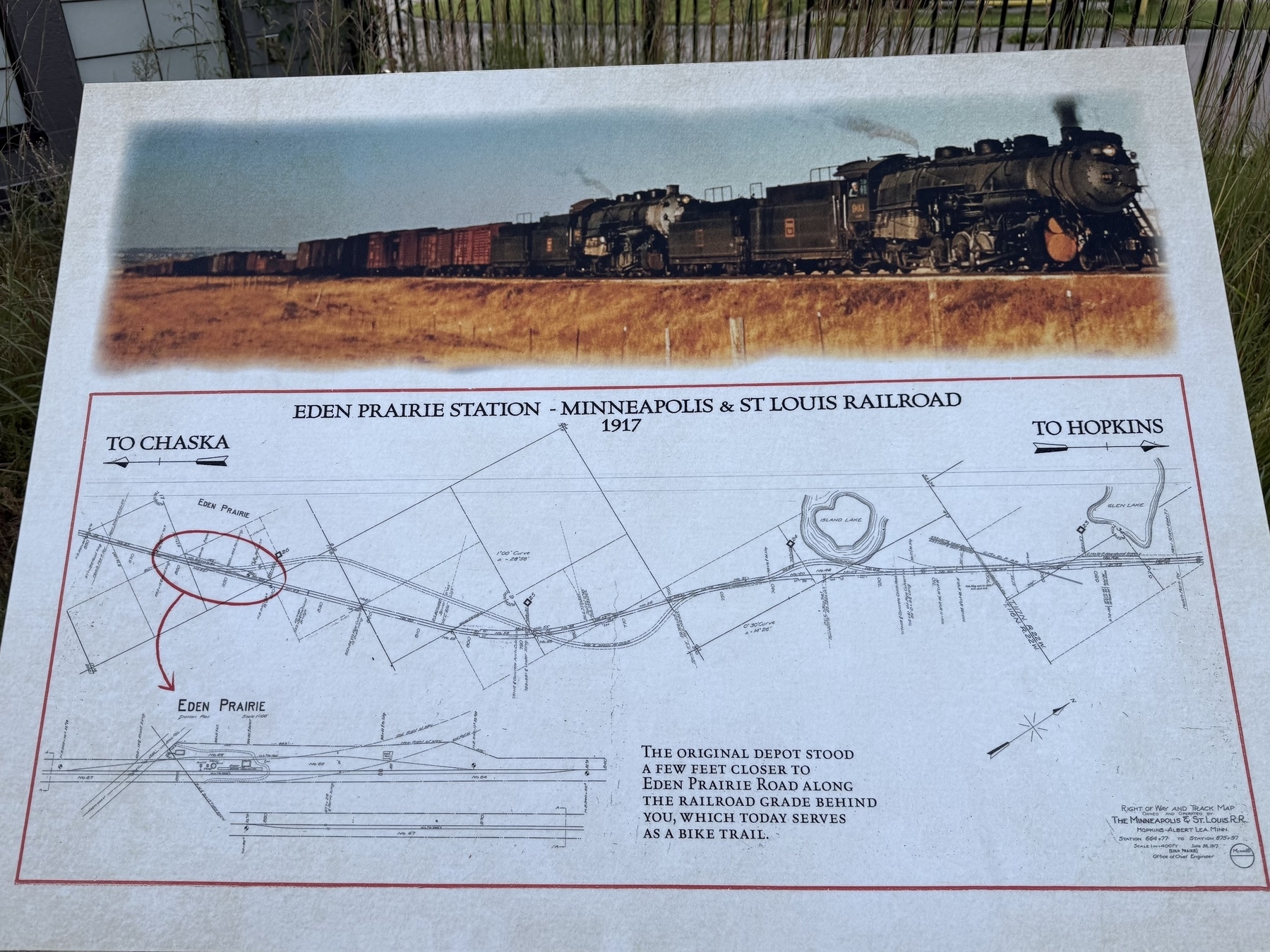 A historical information board showing a black and white map of the Eden Prairie Station on the Minneapolis & St. Louis Railroad from 1917. Above the map is a sepia-toned image of a steam locomotive pulling a train through a landscape. Text on the board explains the location and route of the