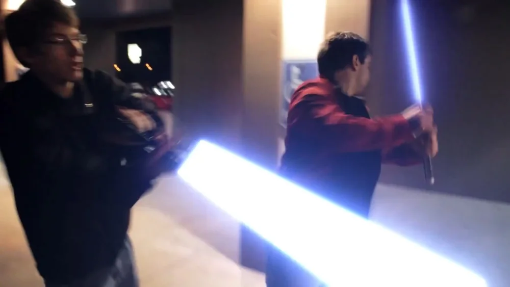 Two people are engaged in a mock lightsaber duel, with glowing blades.