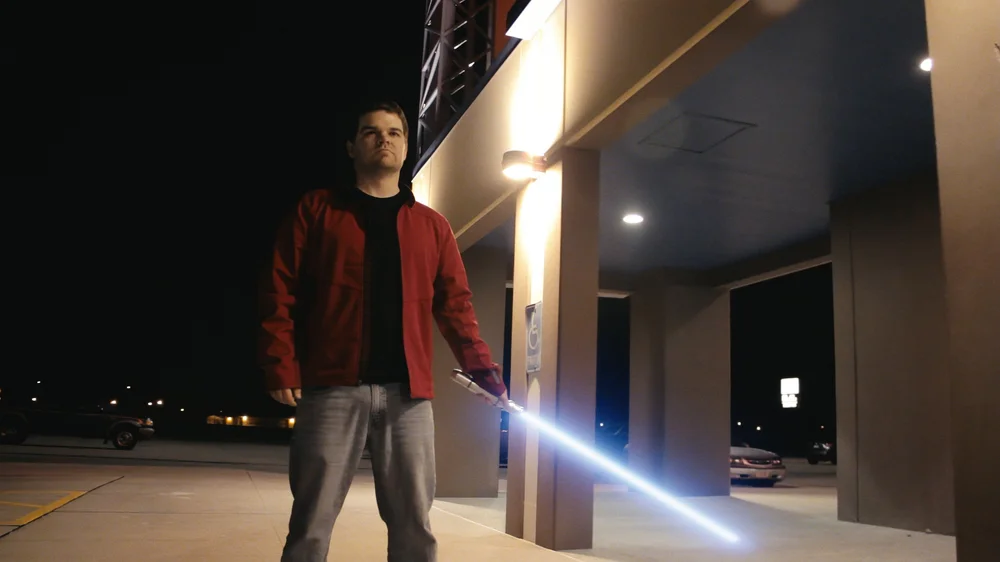 A person is standing in a dimly lit area holding a glowing, blue lightsaber-like object.