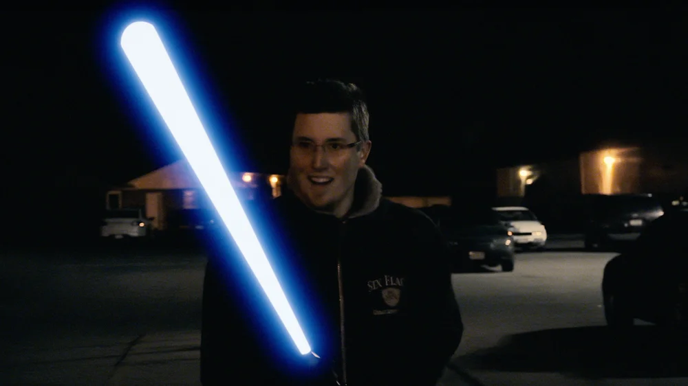 A person is standing outdoors at night holding a glowing blue lightsaber-like object.