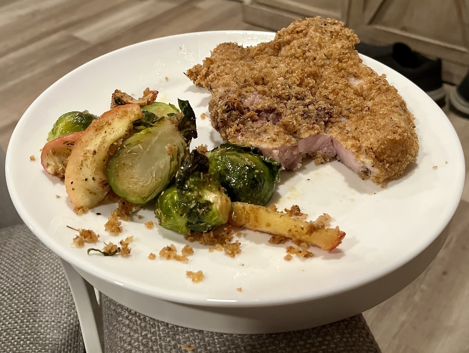 Panko crusted pork chop with roasted apple and Brussels sprouts on a white plate. 