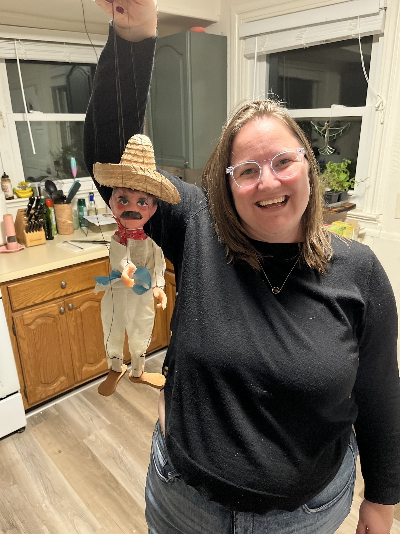 Woman holding a marionette of a man with a mustache and hat. 