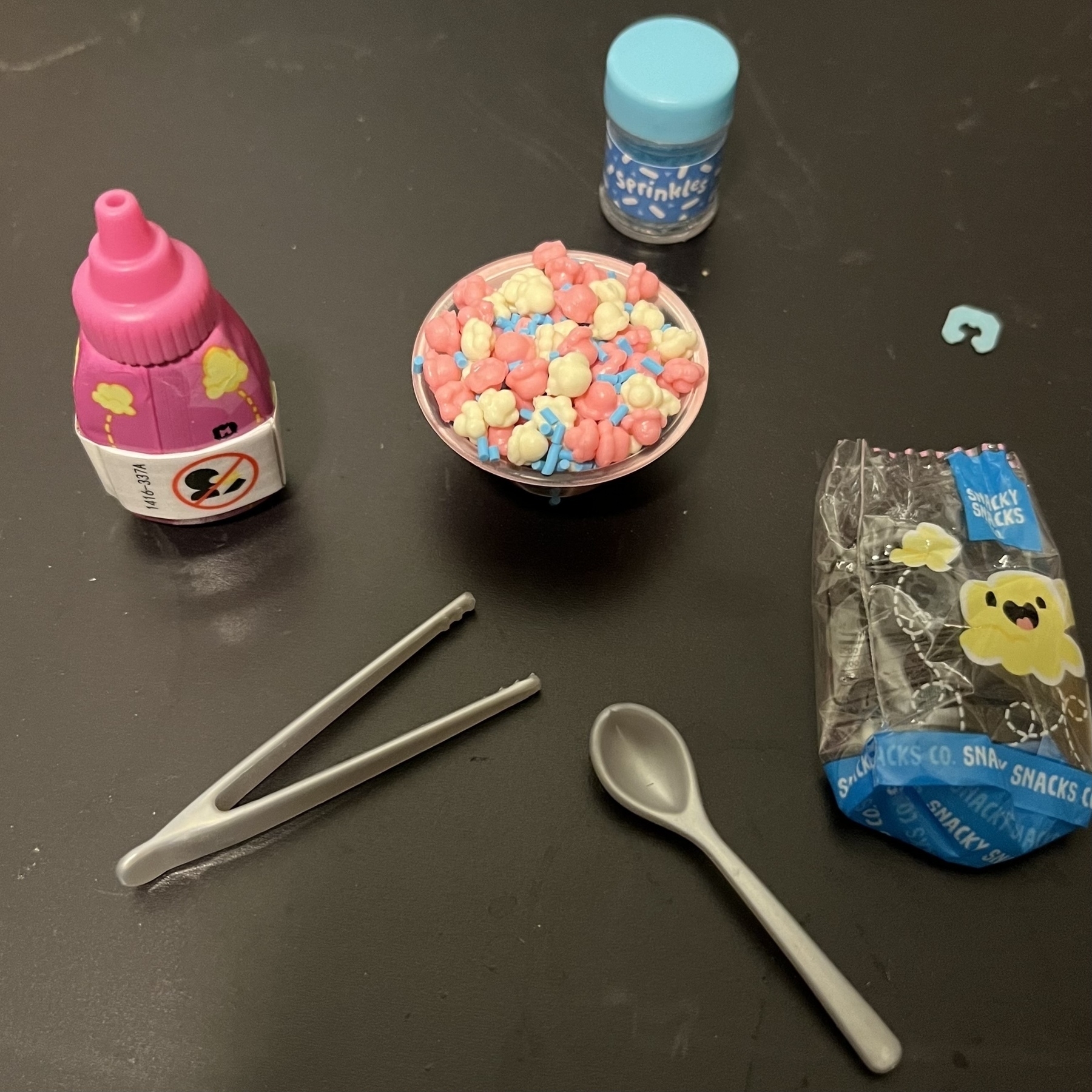 Tiny bowl of plastic popcorn with tweezers, a tiny spoon, popcorn bag and a bottle of resin. 