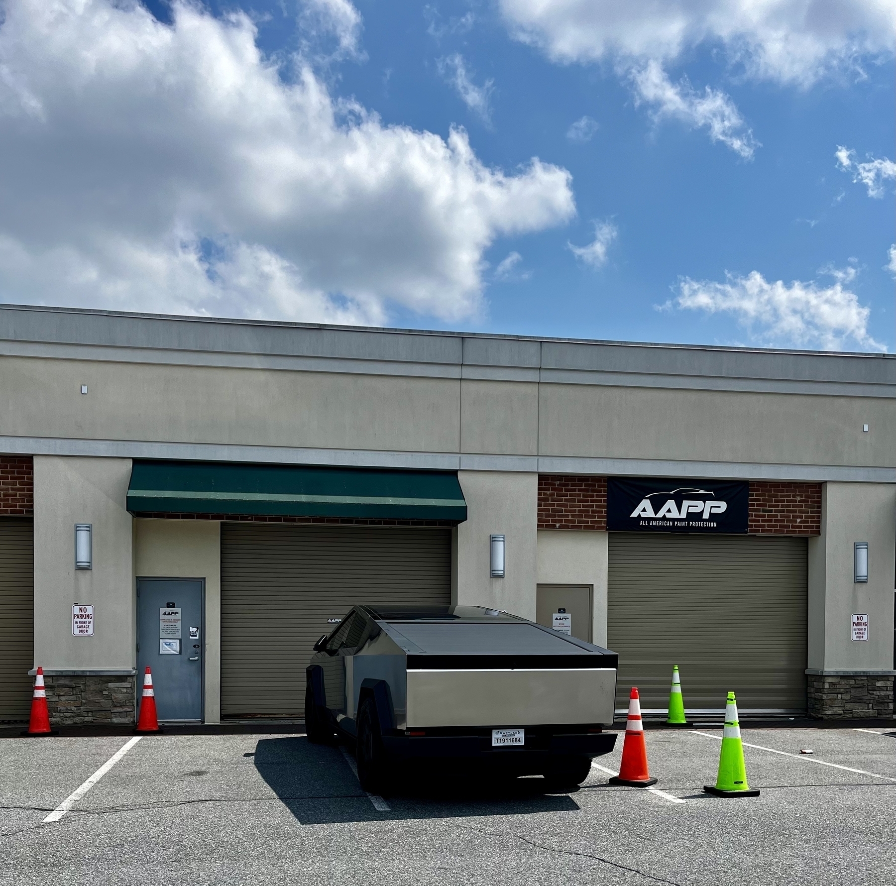 A distinctive angular vehicle (cyber truck) is parked outside a building under a cloudy sky. The cyber truck is nearly the same color as the building. 