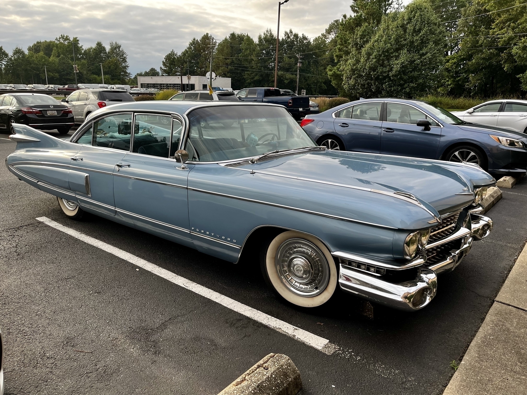 A vintage blue Cadillac is parked in a lot with modern cars. 