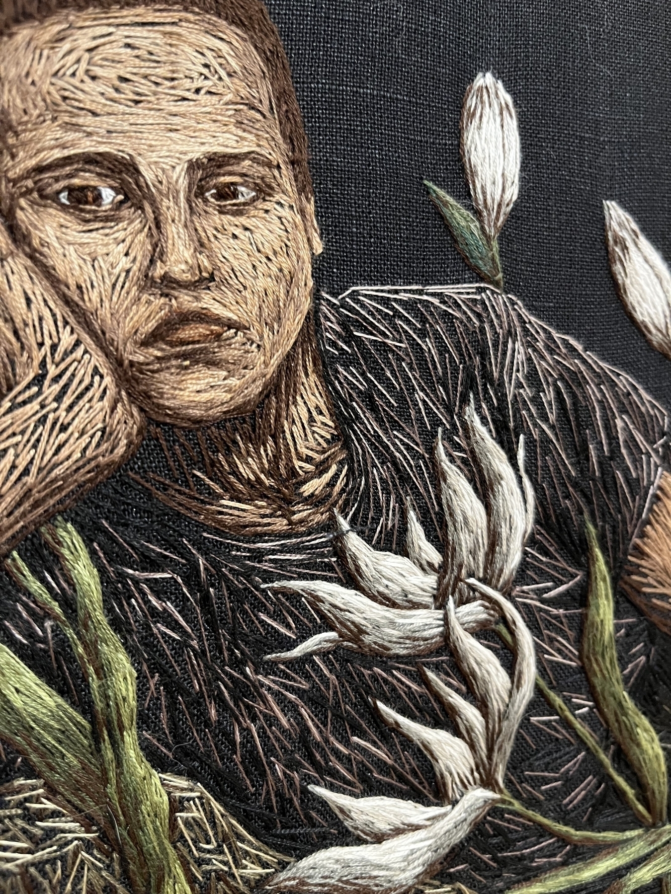 A detailed embroidery of a human face and flowers, with high textural contrast against a dark background.