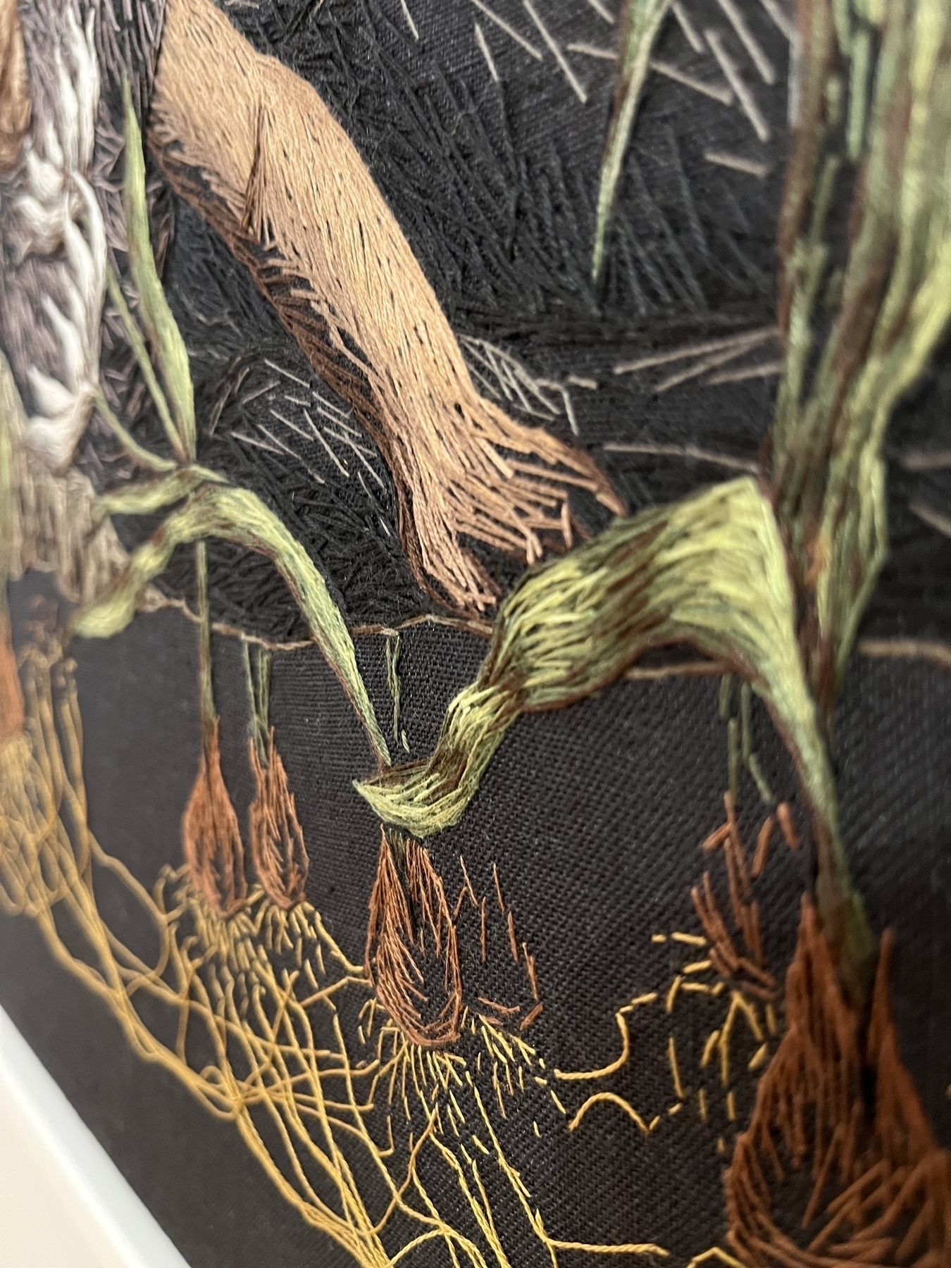 Embroidery threads form the shape of a plant or tree on a black background, showcasing textures and colors to create a botanical design.