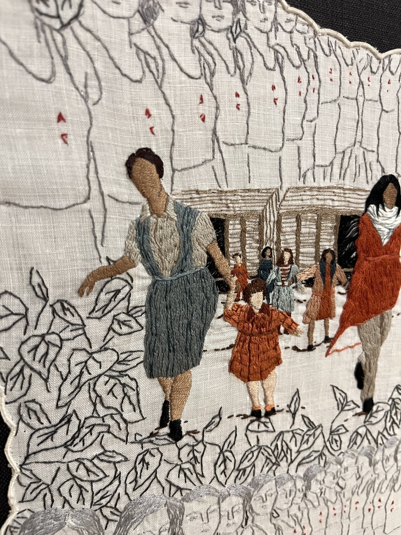 Embroidered figures walking among leaf patterns; a building with people in the background. The scene is depicted in a mix of color and grayscale stitchwork on fabric.