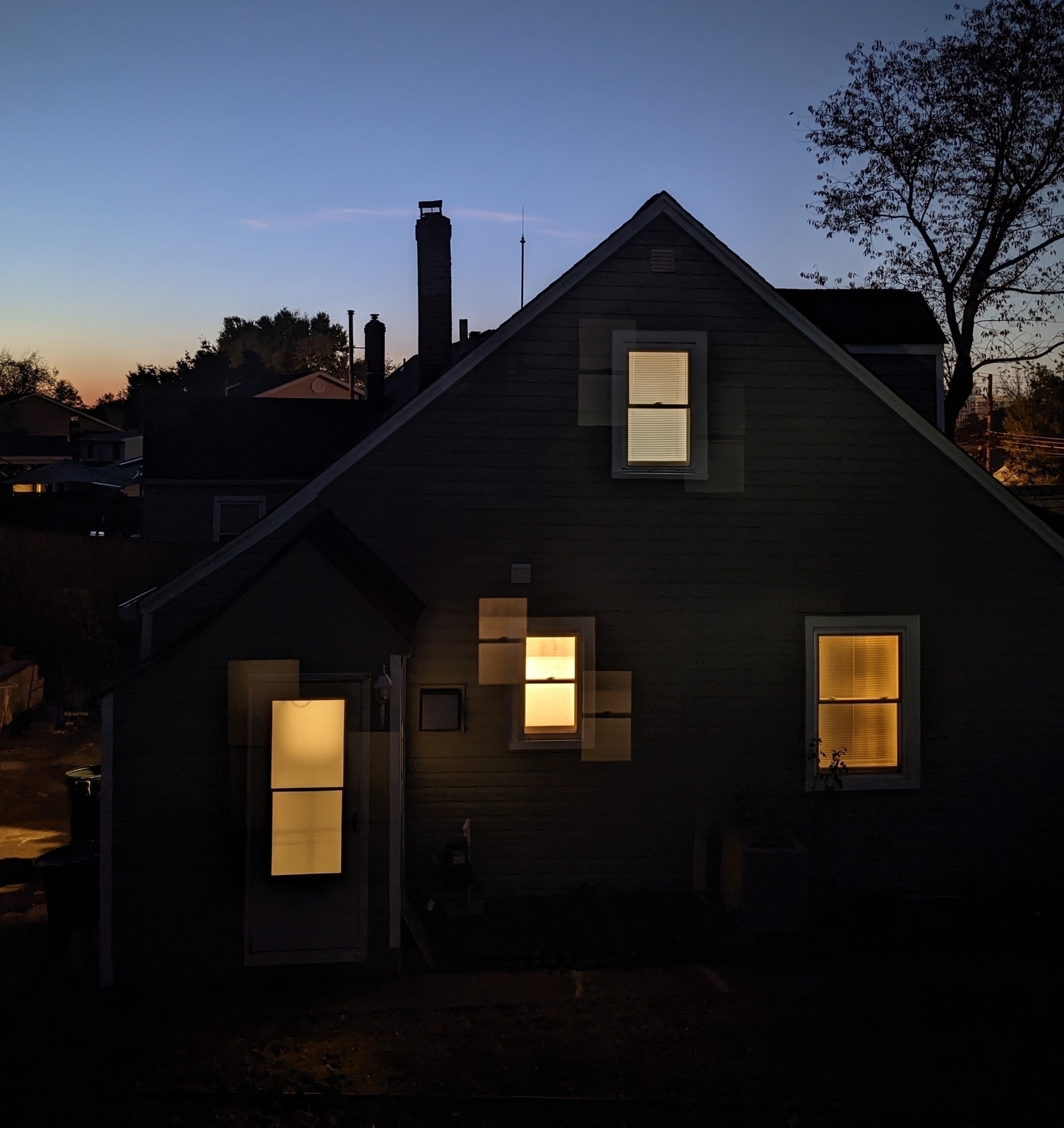 A darkened house with illuminated windows stands against a twilight sky.