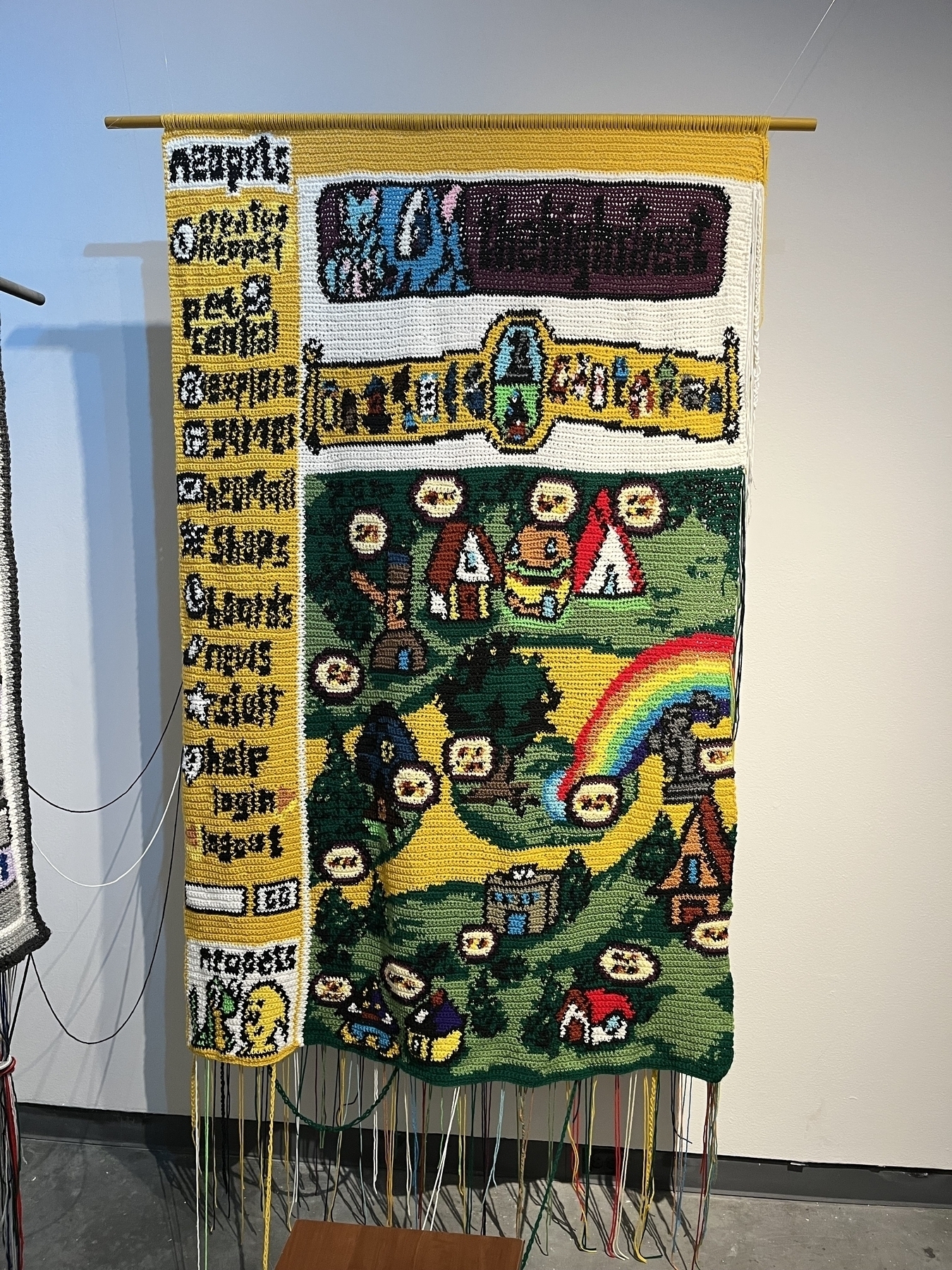 A crocheted tapestry depicts a colorful fantasy village from neopets. 