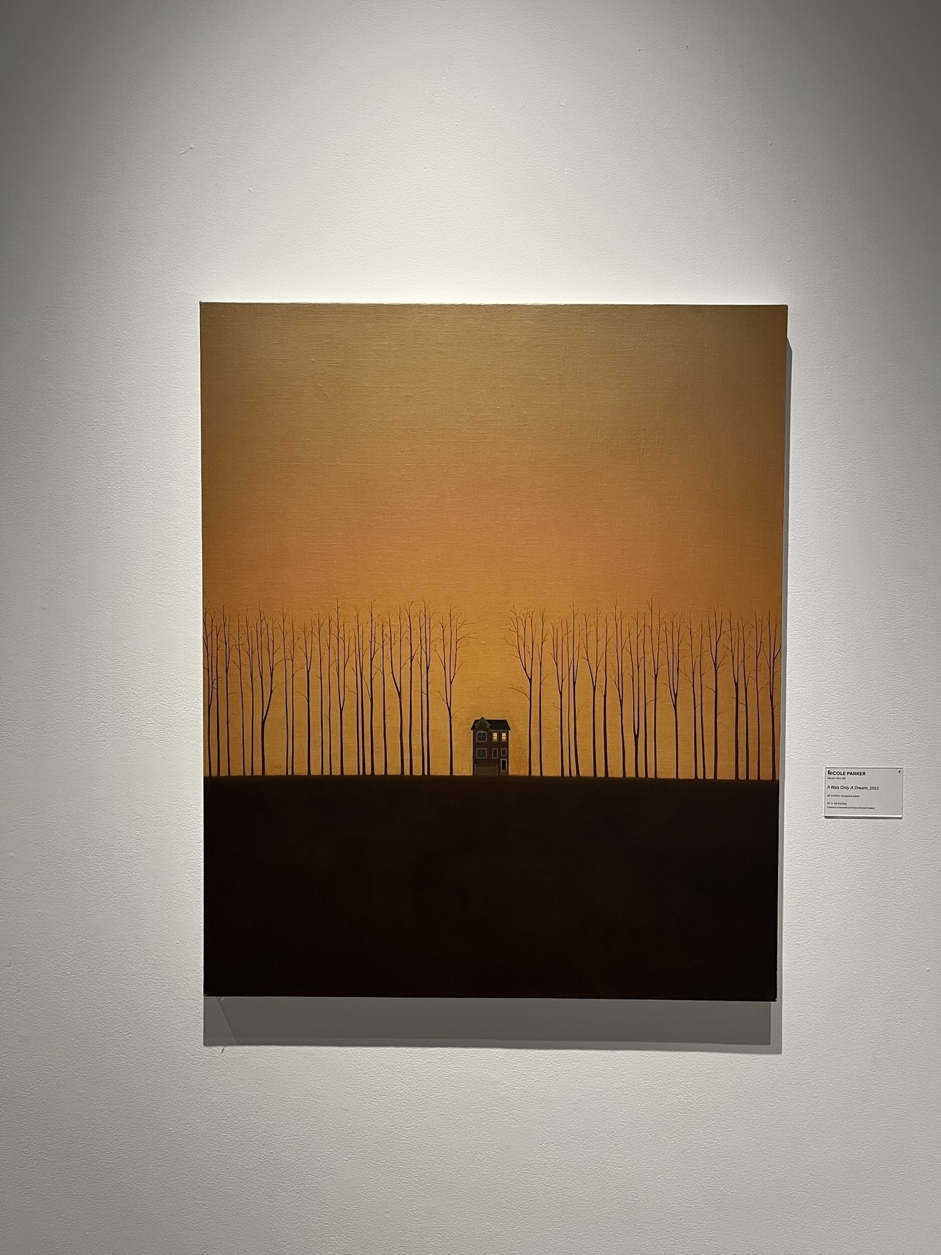 A painting depicts a lone house amid tall, bare trees under a warm, fading yellow sky. It is displayed on a gallery wall, labeled “Nicole Parker, The City of Ember, 2023.”