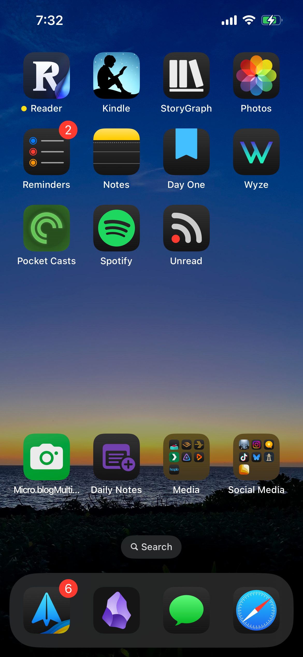 Smartphone home screen displaying various app icons like Reader, Kindle, Reminders, and Spotify. Notifications appear for Reminders and email. Background shows a serene ocean sunset with a search bar. Time reads 7:32.