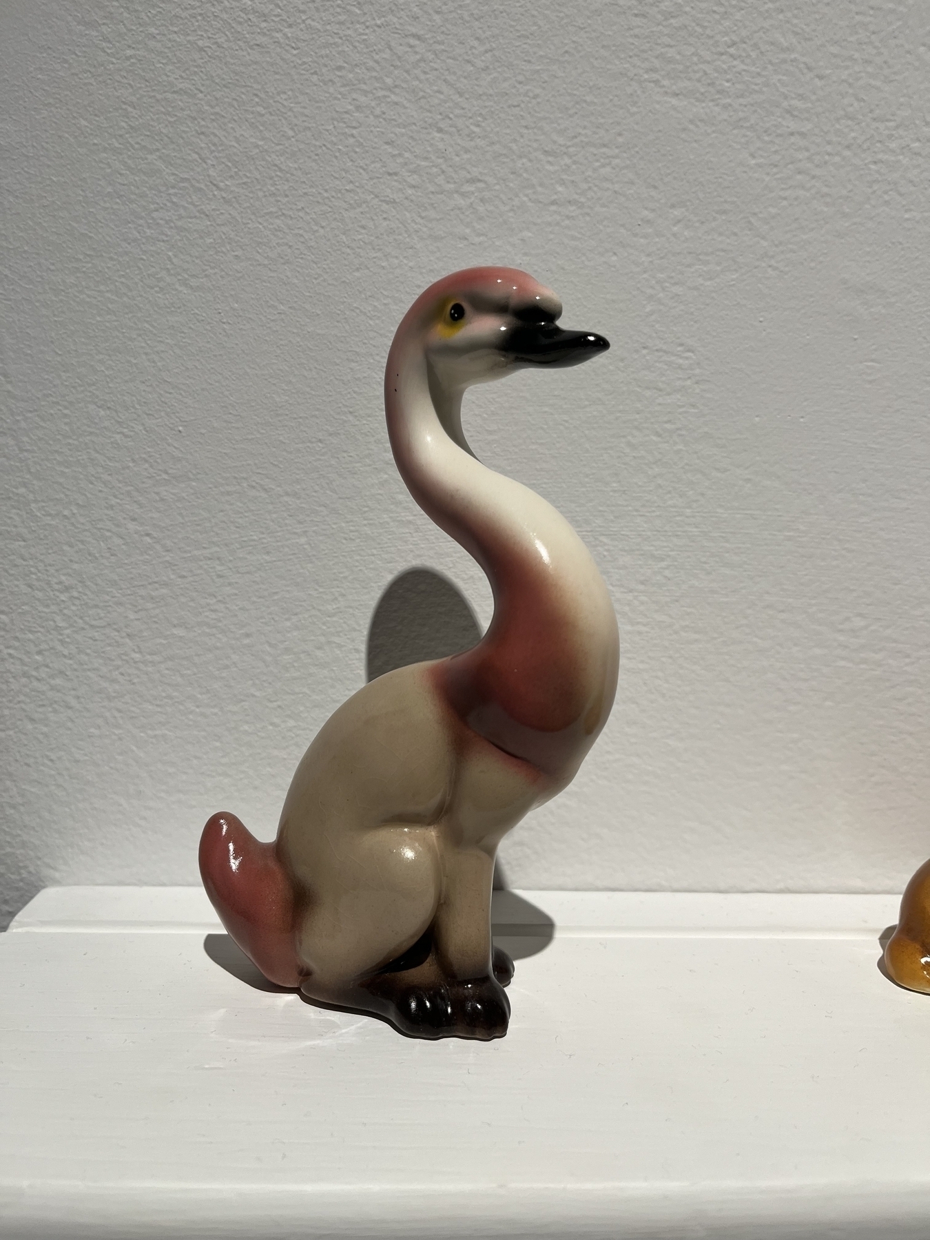 A ceramic figurine of a flamingos neck and head on the body of a brown dog sitting on a shelf. 