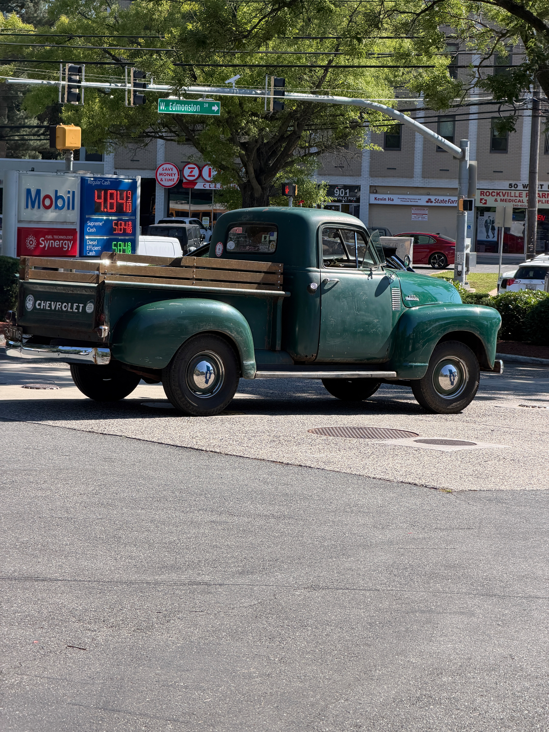 Green vintage Chevrolet truck parked under a tree, at Mobil gas station with a sign displaying prices: Regular 4.09, Super 5.09, Diesel 5.04.