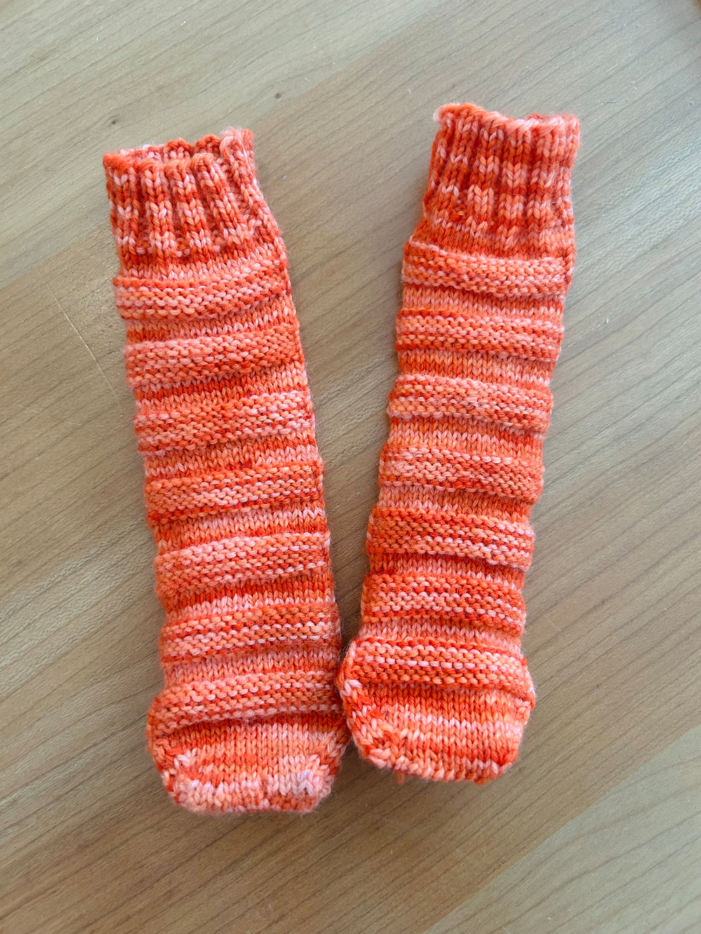 A pair of hand-knitted, orange and pink striped socks are laid out on a wooden surface.