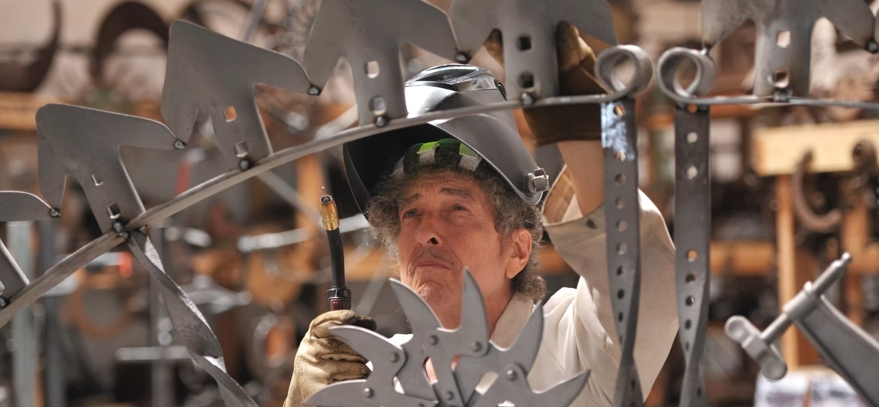 Bob Dylan wearing a welding helmet while working on intricate metal artwork.