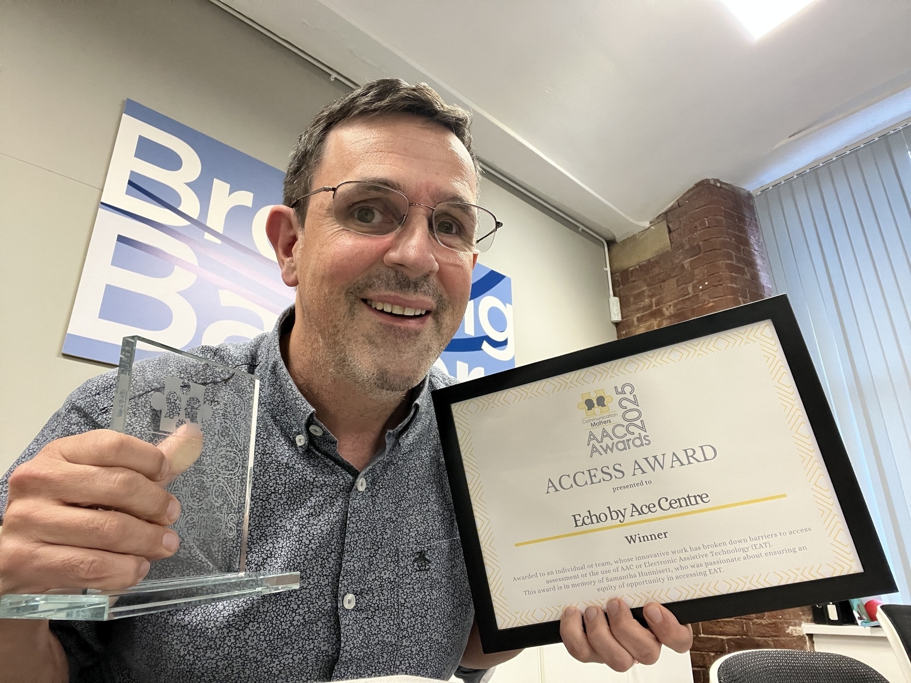 A man is smiling while holding a clear award and a winner certificate for the Access Award from 2023.