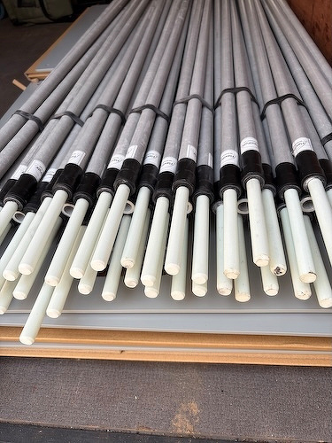 A stack of long metal pipes with white ends is neatly arranged and tied together with black bands.