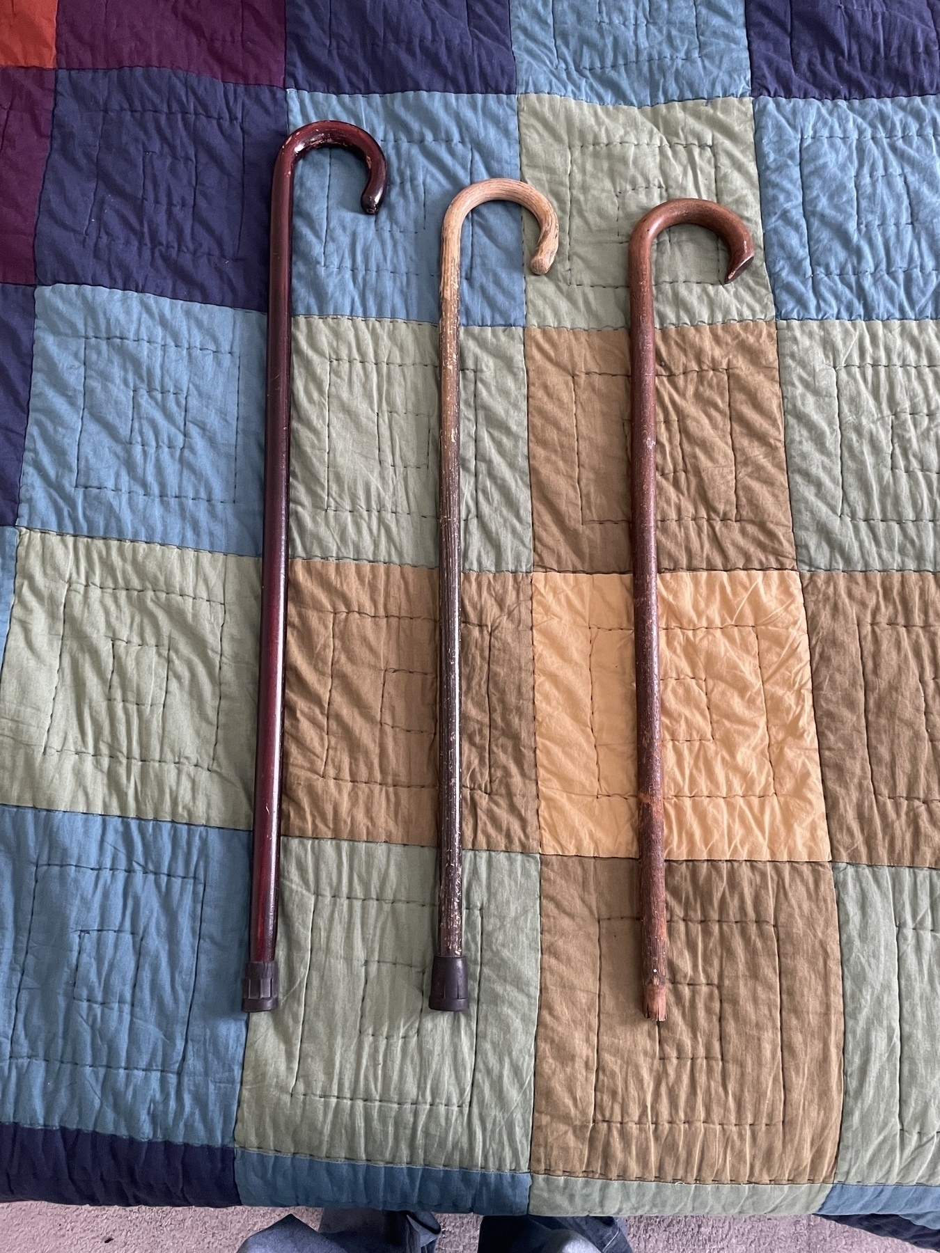 On a geometrically colored quilt, three wooden canes are laid in descending order of height. All are worn; the third is missing a rubber foot. 