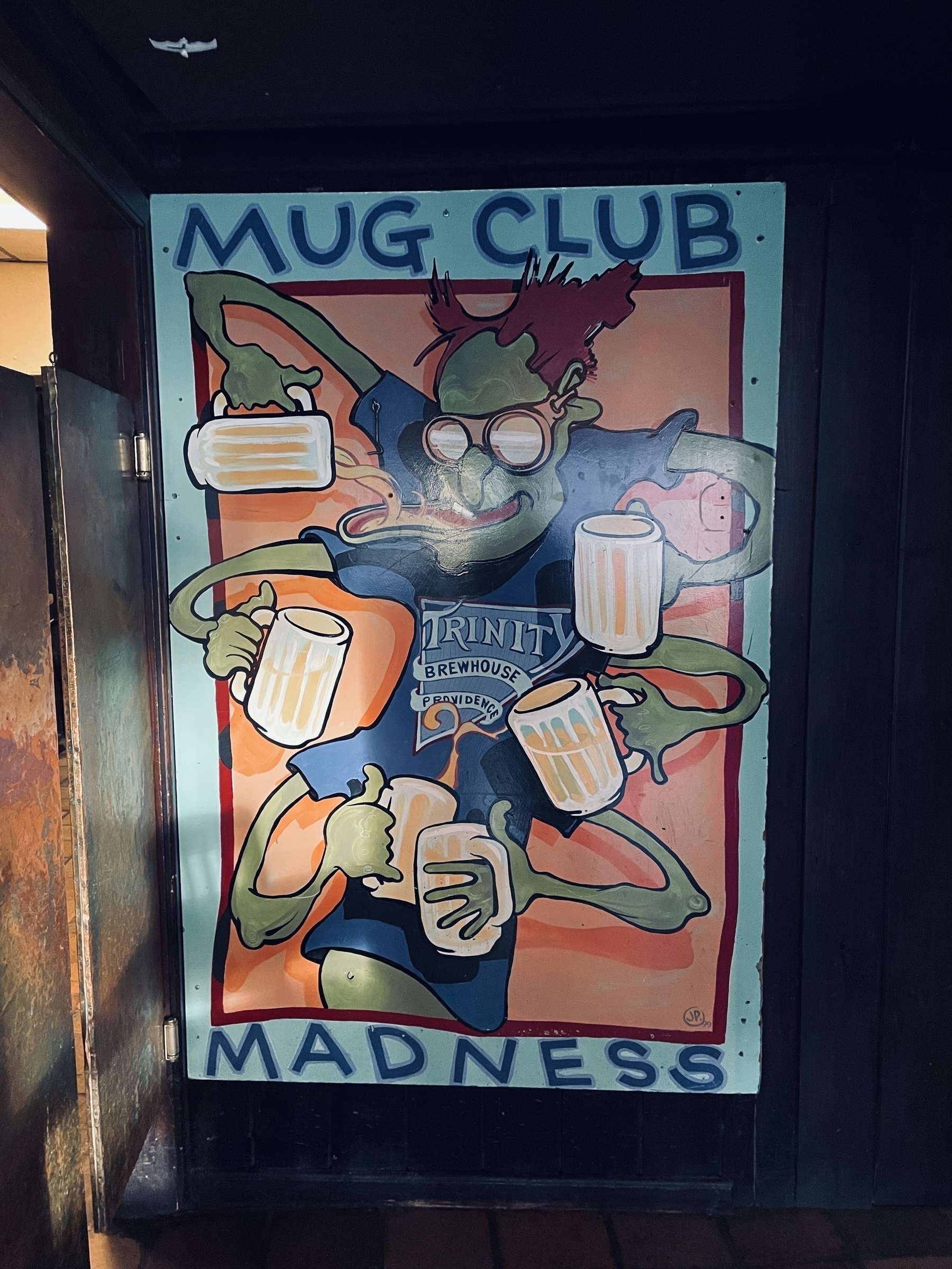 A painted wall art of a six-armed green monster, a pint of beer in each hand, wearing a blue T-shirt with the Trinity Brewhouse logo. Above and below the picture are the words “Mug House Madness”.