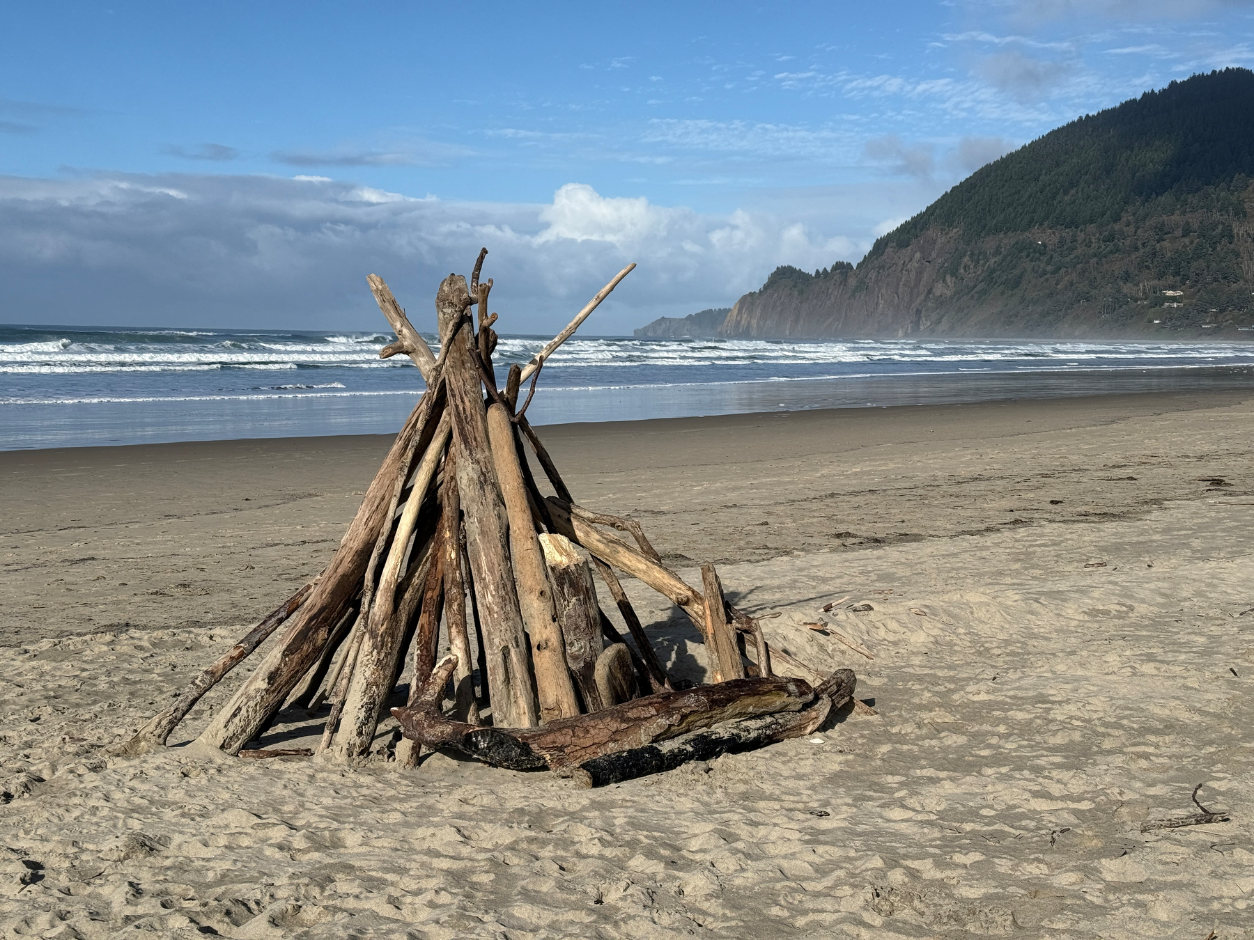 Beach fort pyramid of driftwood, waves and mountain in the background 