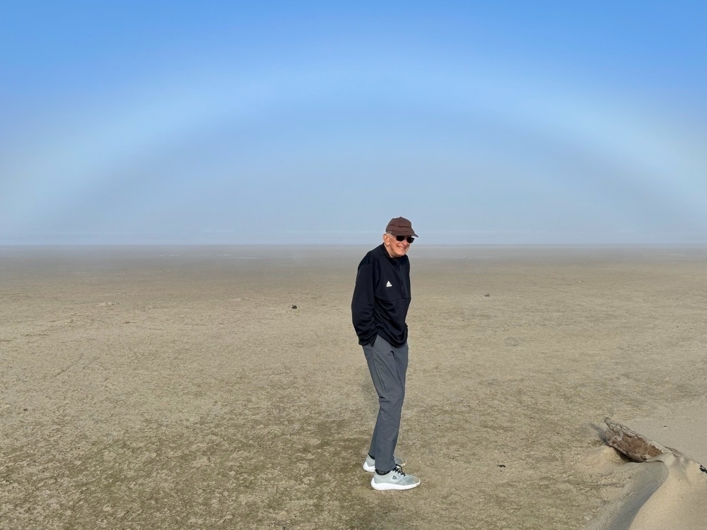 old man on the beach with a white rainbow above him