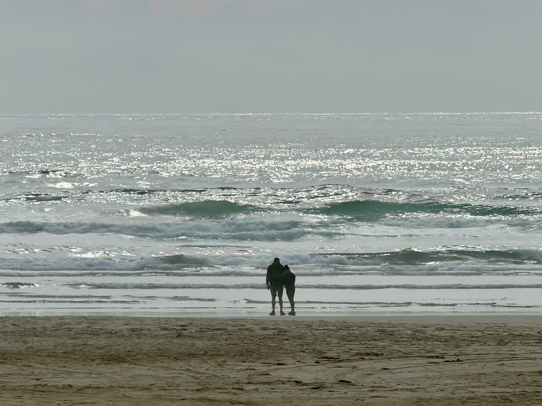 The sun glinting off the Pacific ocean on an overcast day, a couple silhouetted 