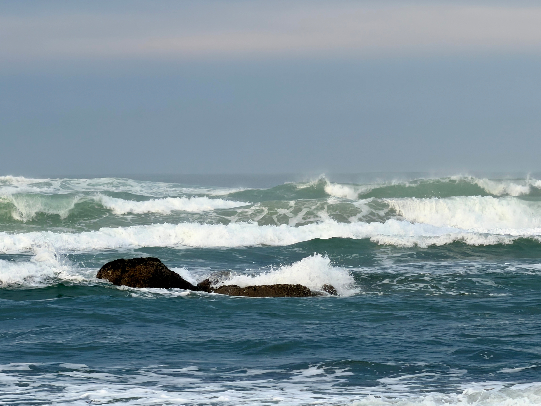 Waves breaking over a rock in the Pacific Ocean, overcast skies. 