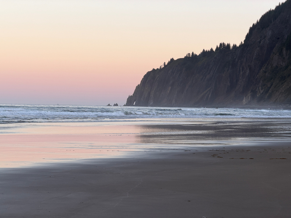 Dark mountain cliff and wet sand offsetting dawn colors. 