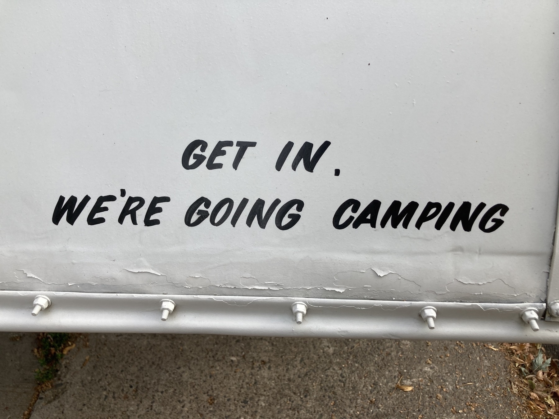 "Get In, We're Going Camping," stenciled on old-school camp trailer