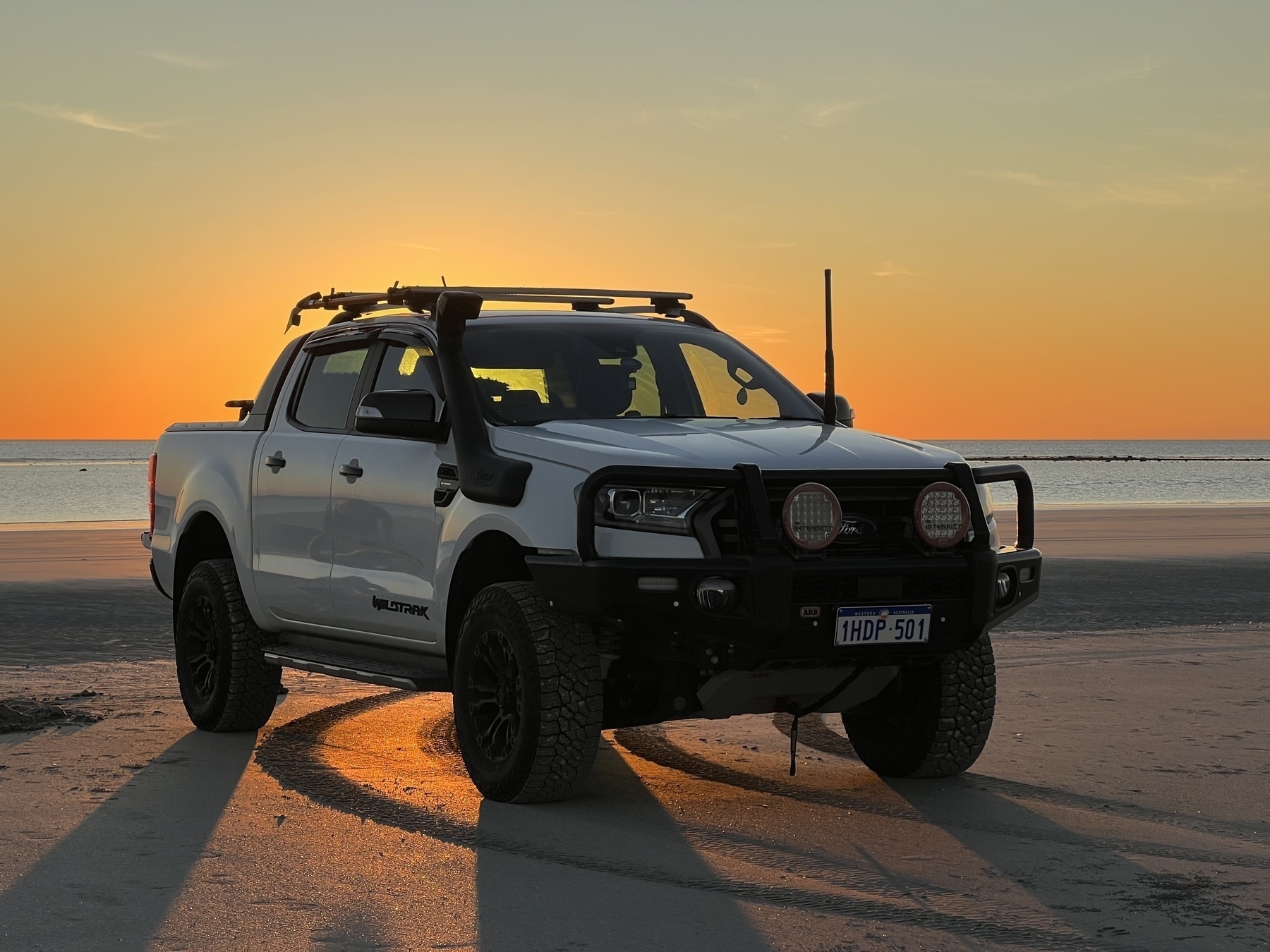 A truck/ute on the beach with the sub setting beging. 