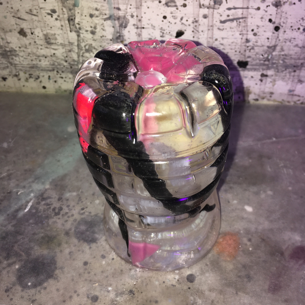 A small, clear glass sculpture with black and dark pinkish-purple swirling patterns stands on a speckled, textured surface.