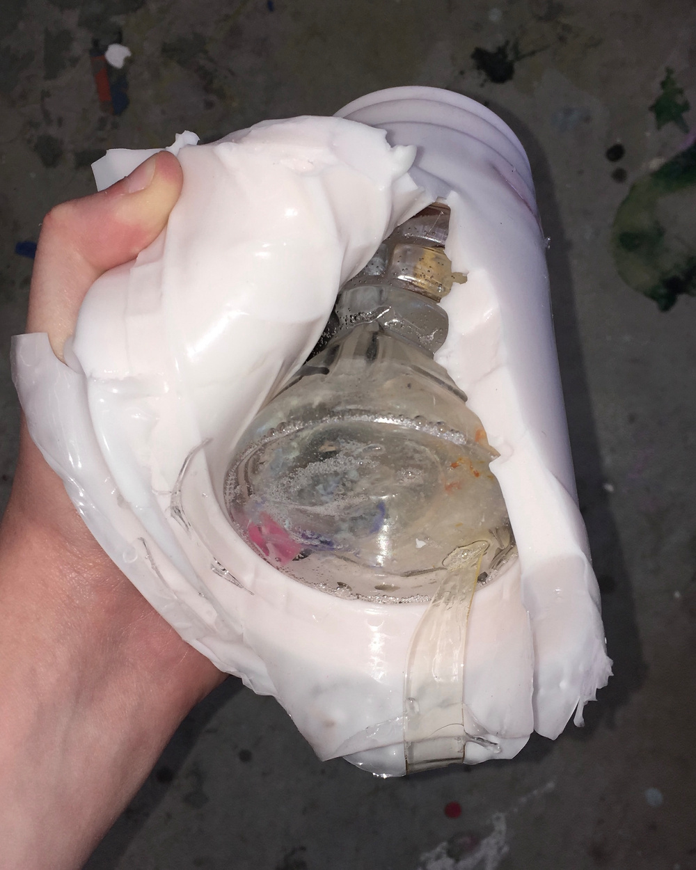 A hand is holding a translucent object with a partially visible bottle inside, wrapped in a white material.