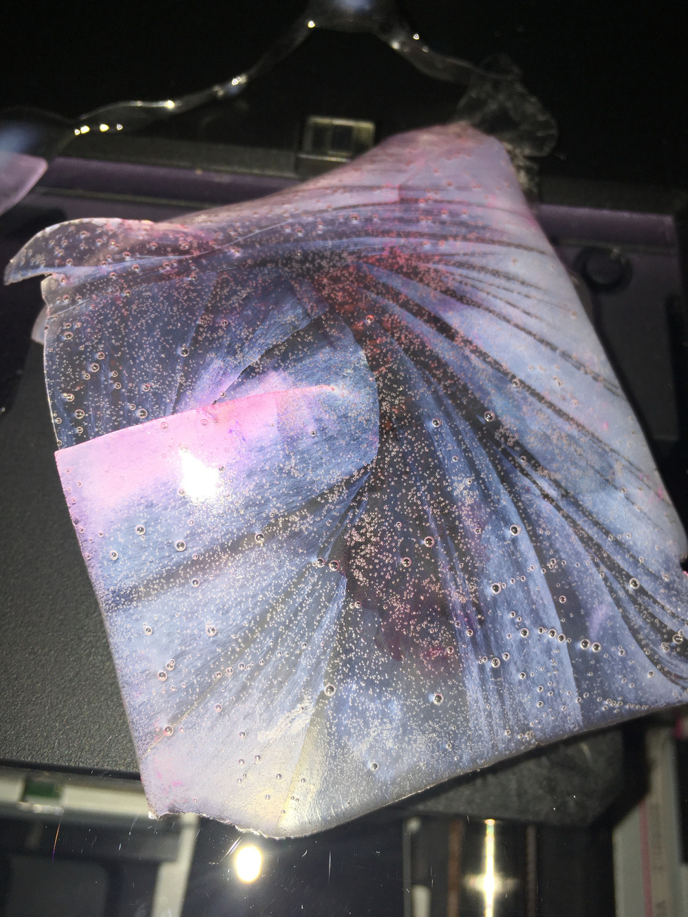 A piece of fabric with a swirling pattern in blue, pink, and purple hues is set against a dark background.