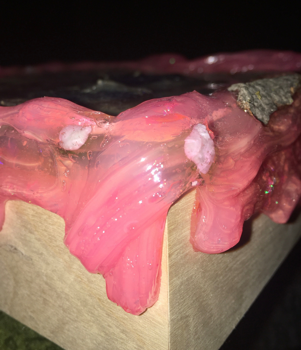 A wooden block is partially covered with glossy, pink resin that appears to be dripping over the edges.