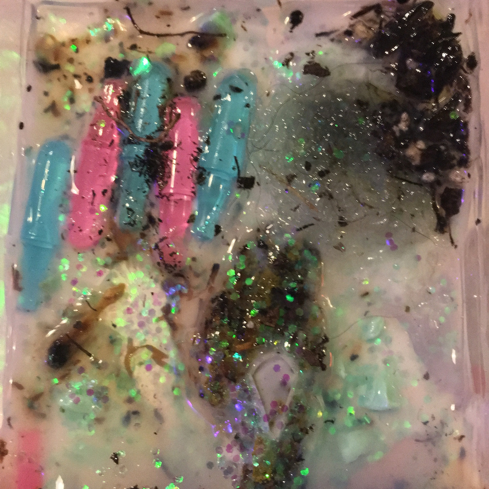 A colorful and abstract mixture of paints, glitter, and various materials creates a textured and chaotic design.